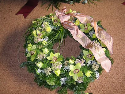 Zöld orchideákkal díszített temetői koszorú rózsaszín szalaggal.