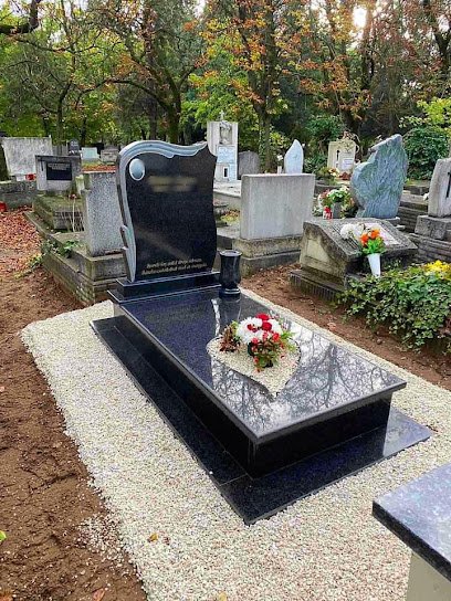 Fekete gránit sírkő, díszes felirattal, kavicságyon.